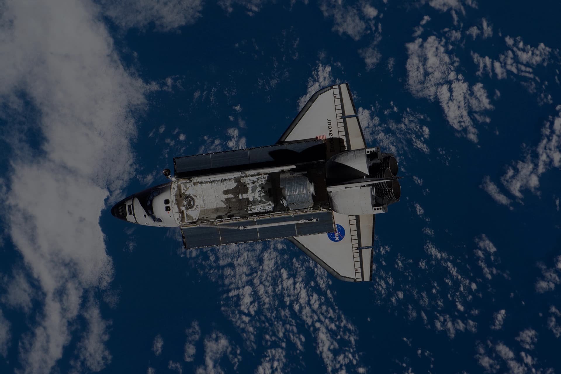 The Space Shuttle Endeavour in orbit above Earth, with its payload bay open and main engines visible.