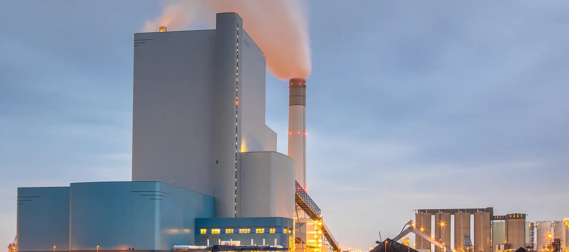 A power plant with a large smokestack and a cooling tower in the background.