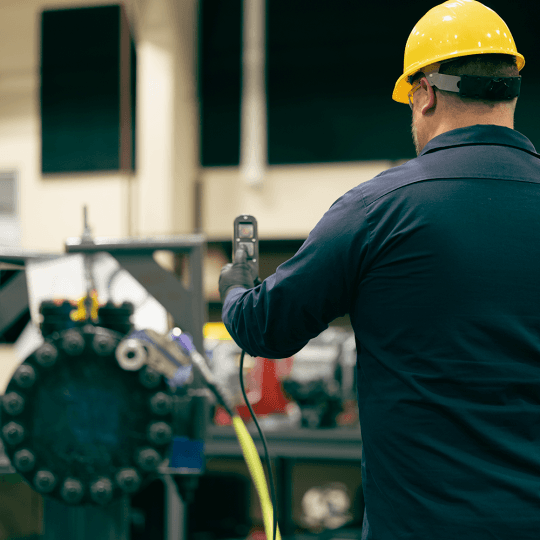 A technician operating a STEALTH Hydraulic Torque Wrench from a distance. He is wearing a hard hat, safety gloves and glasses, and using a remote pendant.