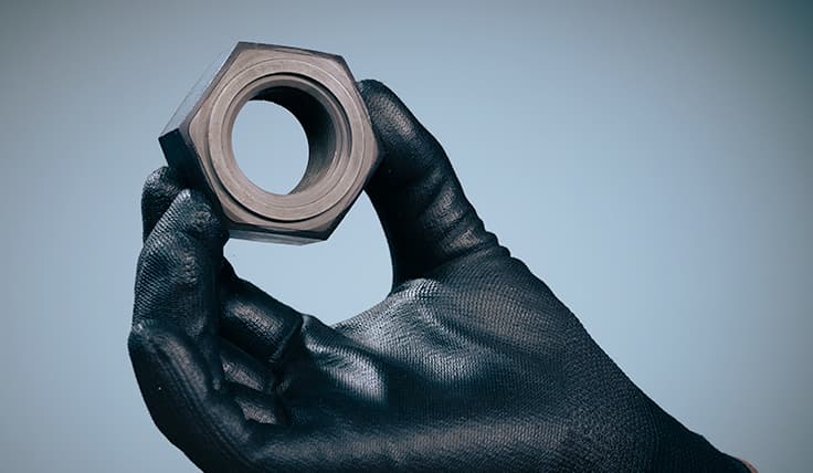 A gloved hand holding a HYTORC Gall-Free Nut, showing the top-side indicator ring and the two-part design.