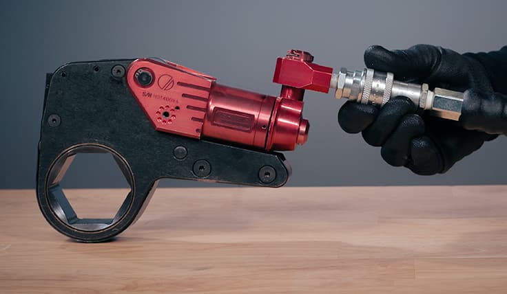 A gloved hand holds the Uniswivel connectors of the XLCT Low Clearance Hydraulic Torque Wrench.